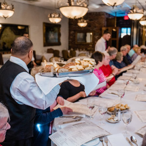 waiter with serving tray of bread at large table of people